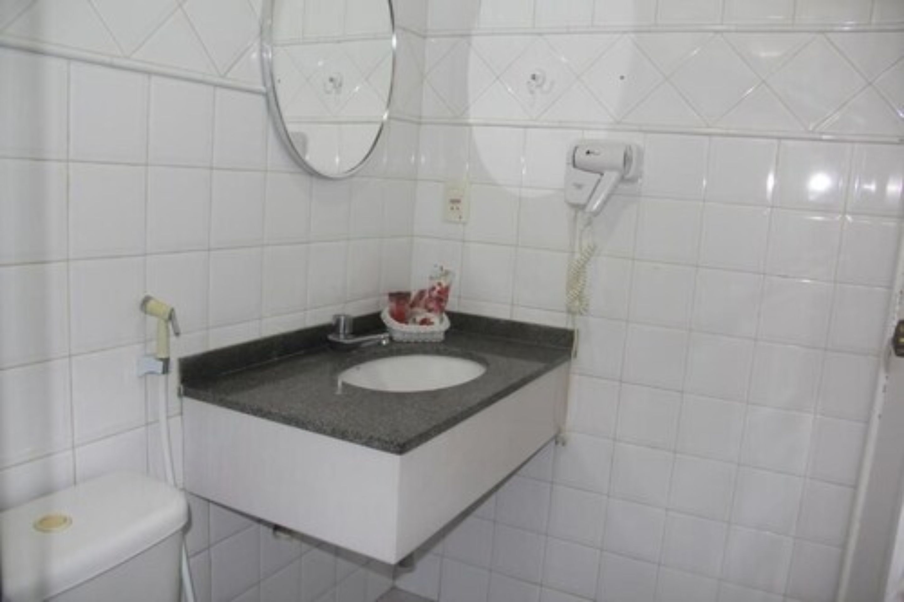 A bathroom with a white toilet, a sink with a granite countertop, a mirror, and a towel rack.
