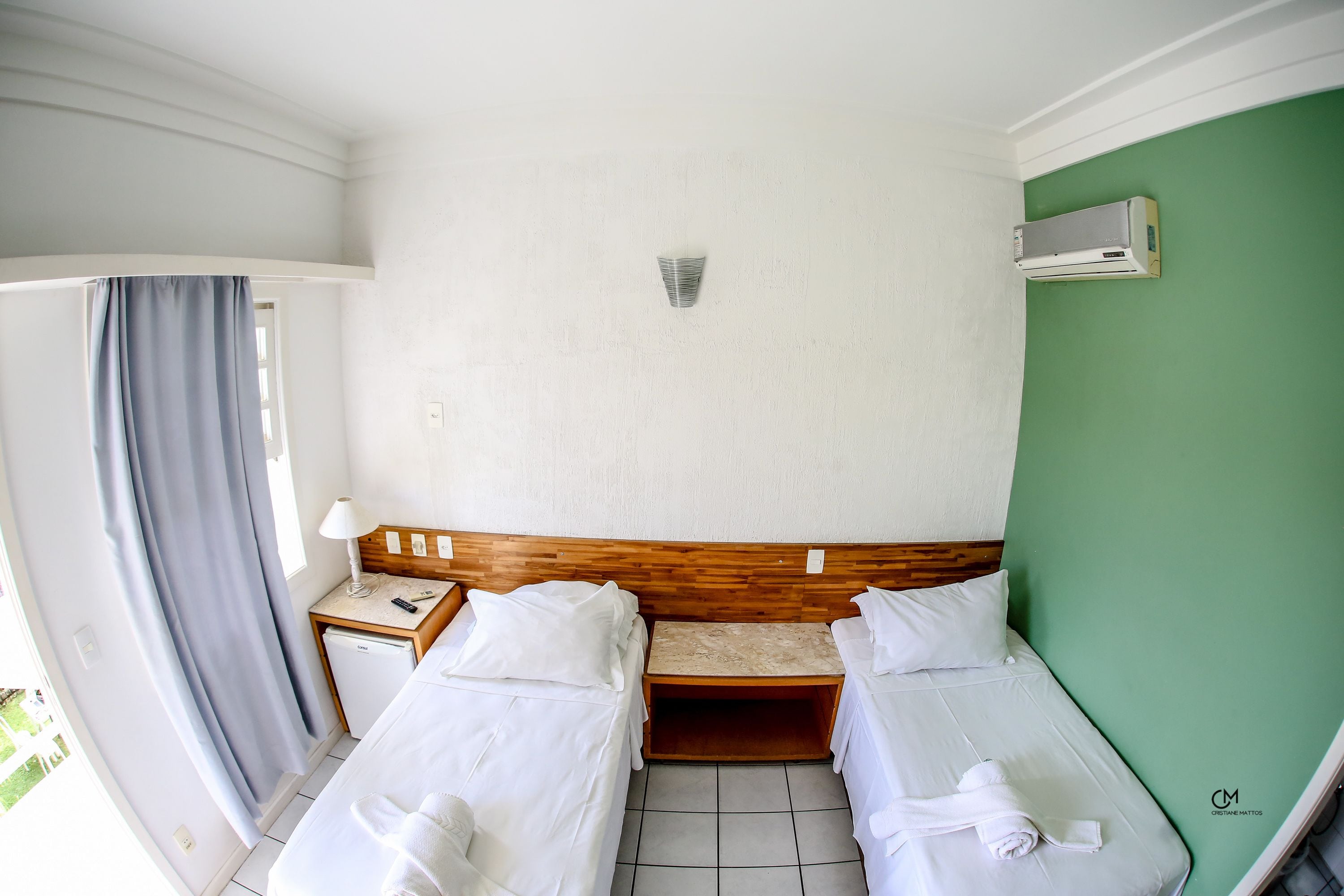 Habitación de hotel con dos camas, una mesita de noche de madera, aire acondicionado en la pared y vistas al exterior.