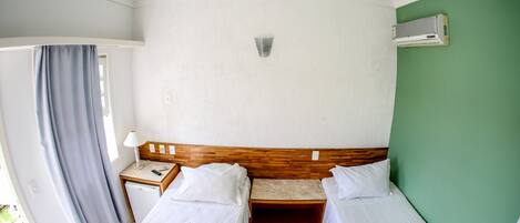 Habitación de hotel con dos camas, una mesita de noche de madera, aire acondicionado en la pared y vistas al exterior.
