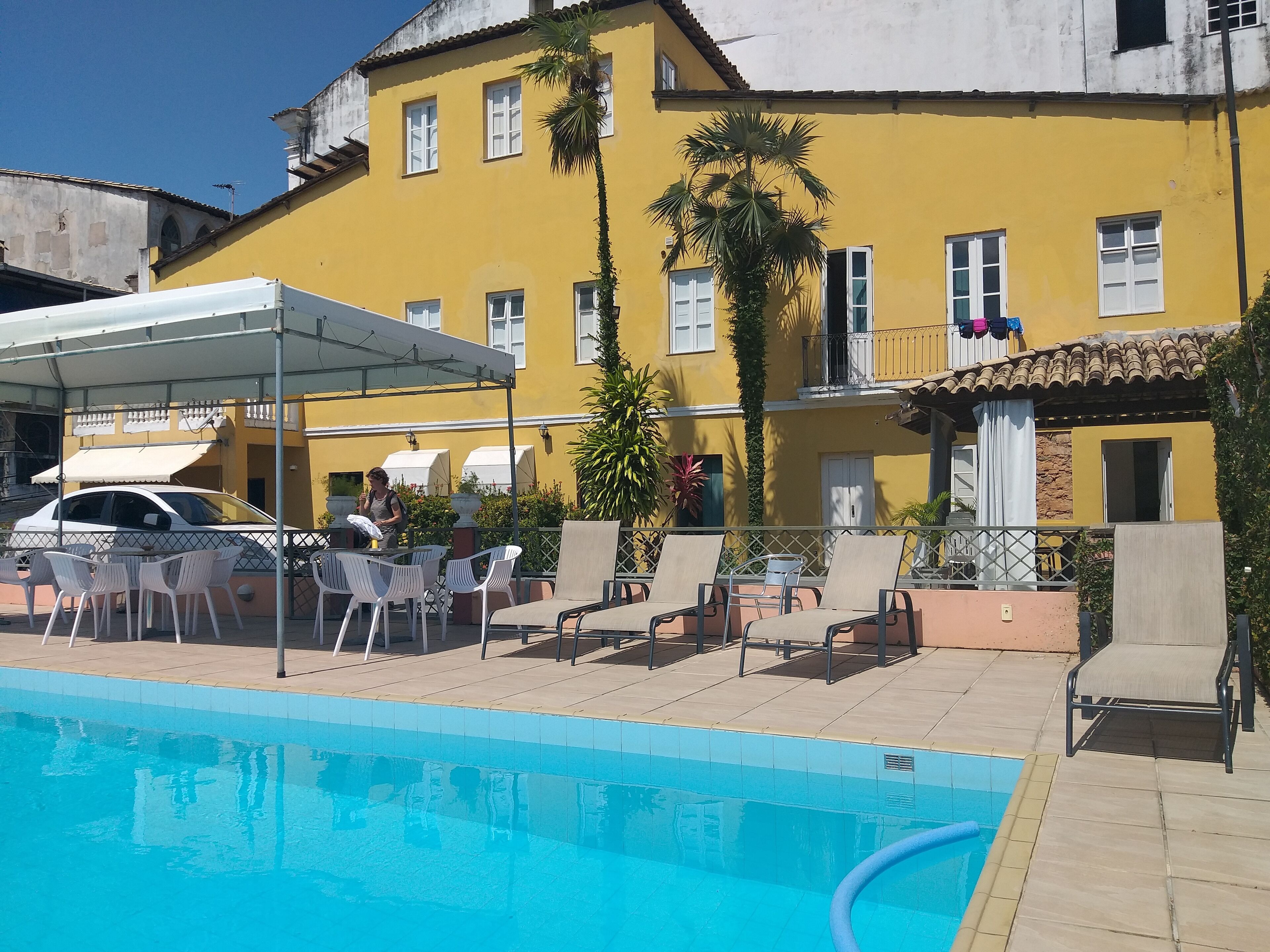 A yellow building with a swimming pool, outdoor seating, and a covered patio area.