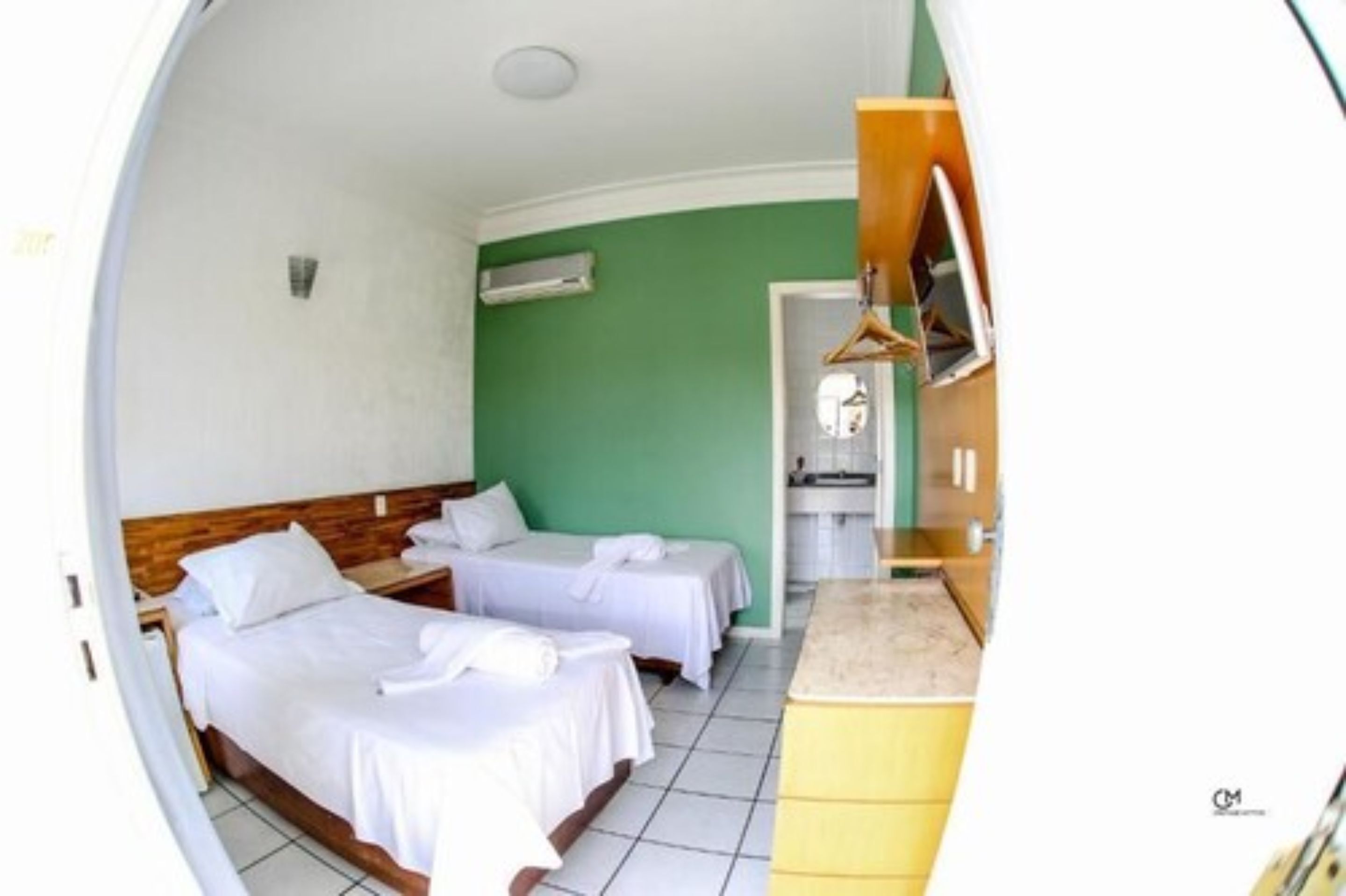 Ein Hotelzimmer mit zwei Betten, einer kleinen Küchenzeile und einem Badezimmer mit Spiegel und Waschbecken.
