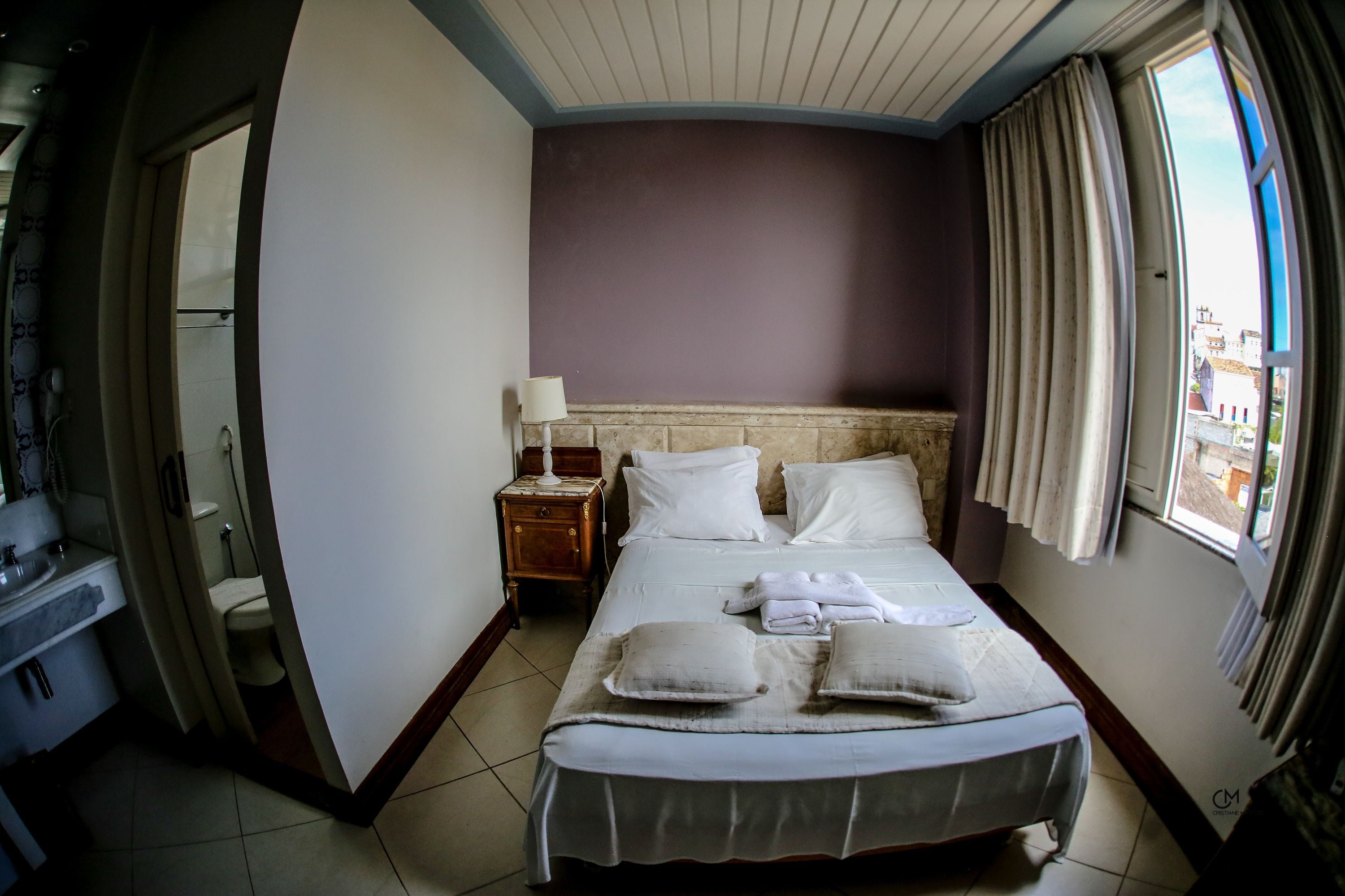 Une chambre d’hôtel avec un lit, une table de chevet, une lampe et une fenêtre avec des rideaux.