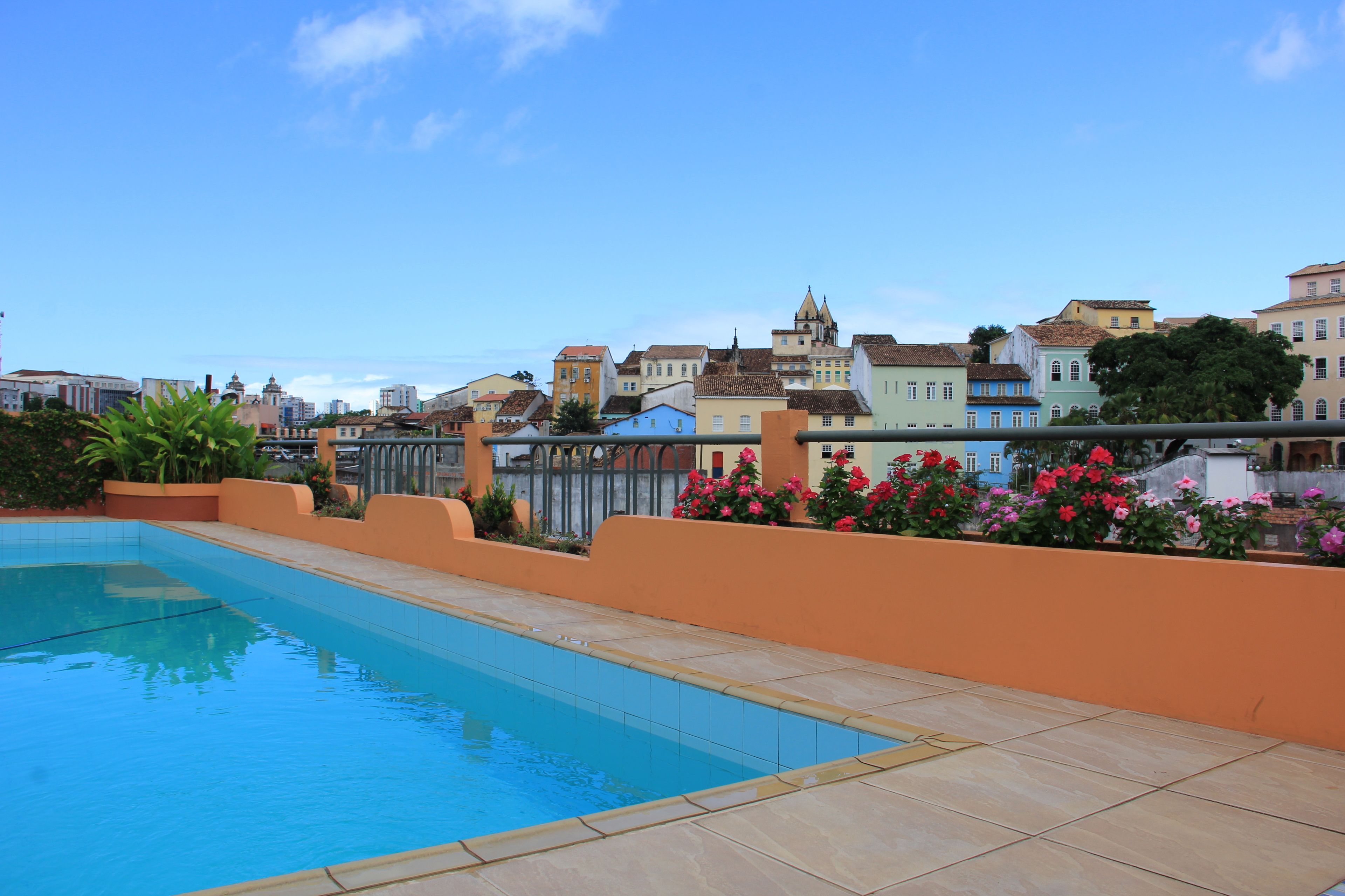 A swimming pool with a tiled edge, surrounded by a low orange wall and a metal fence.