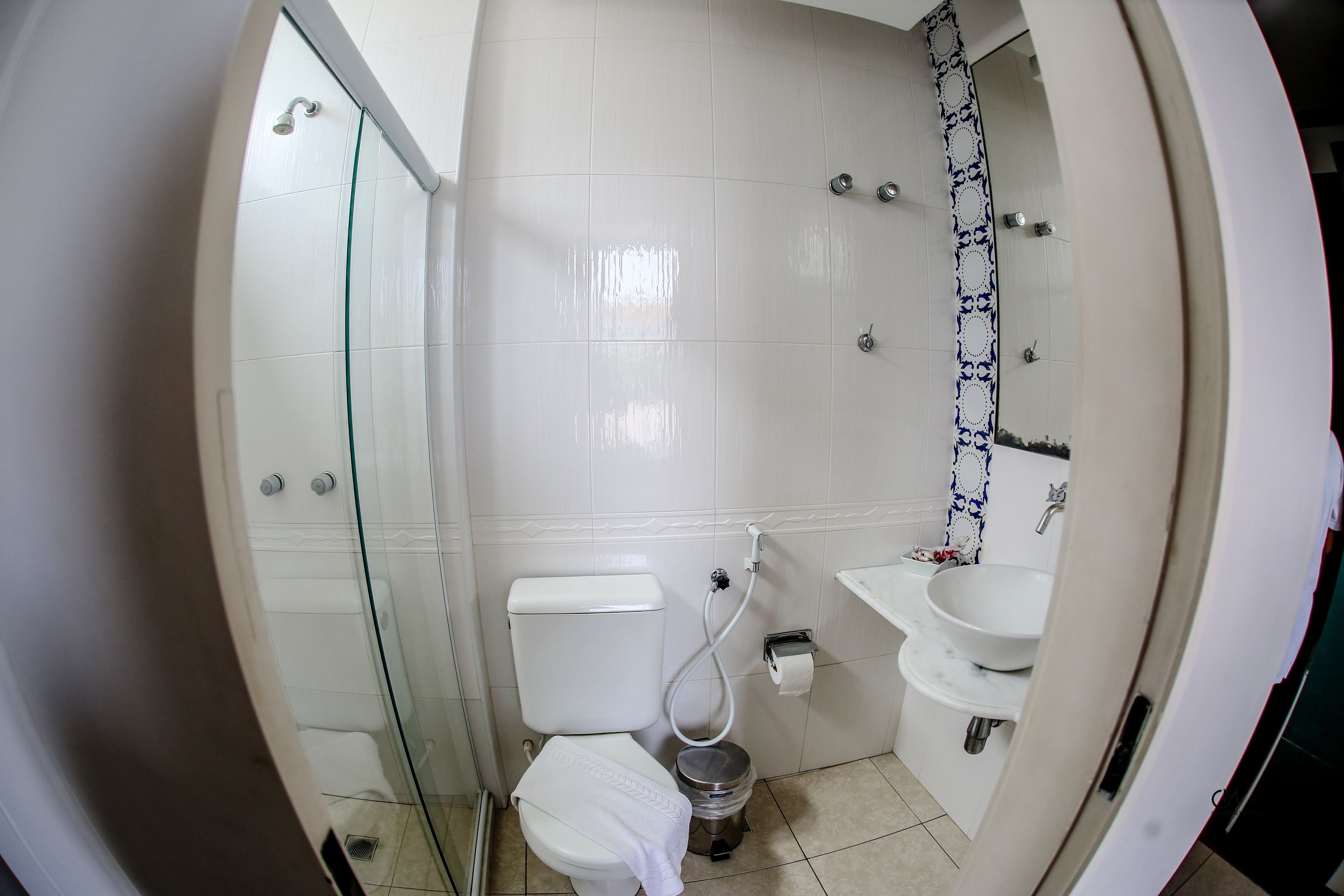 Een badkamer met een douche met glazen wand, toilet, wastafel en een betegelde spatwand.