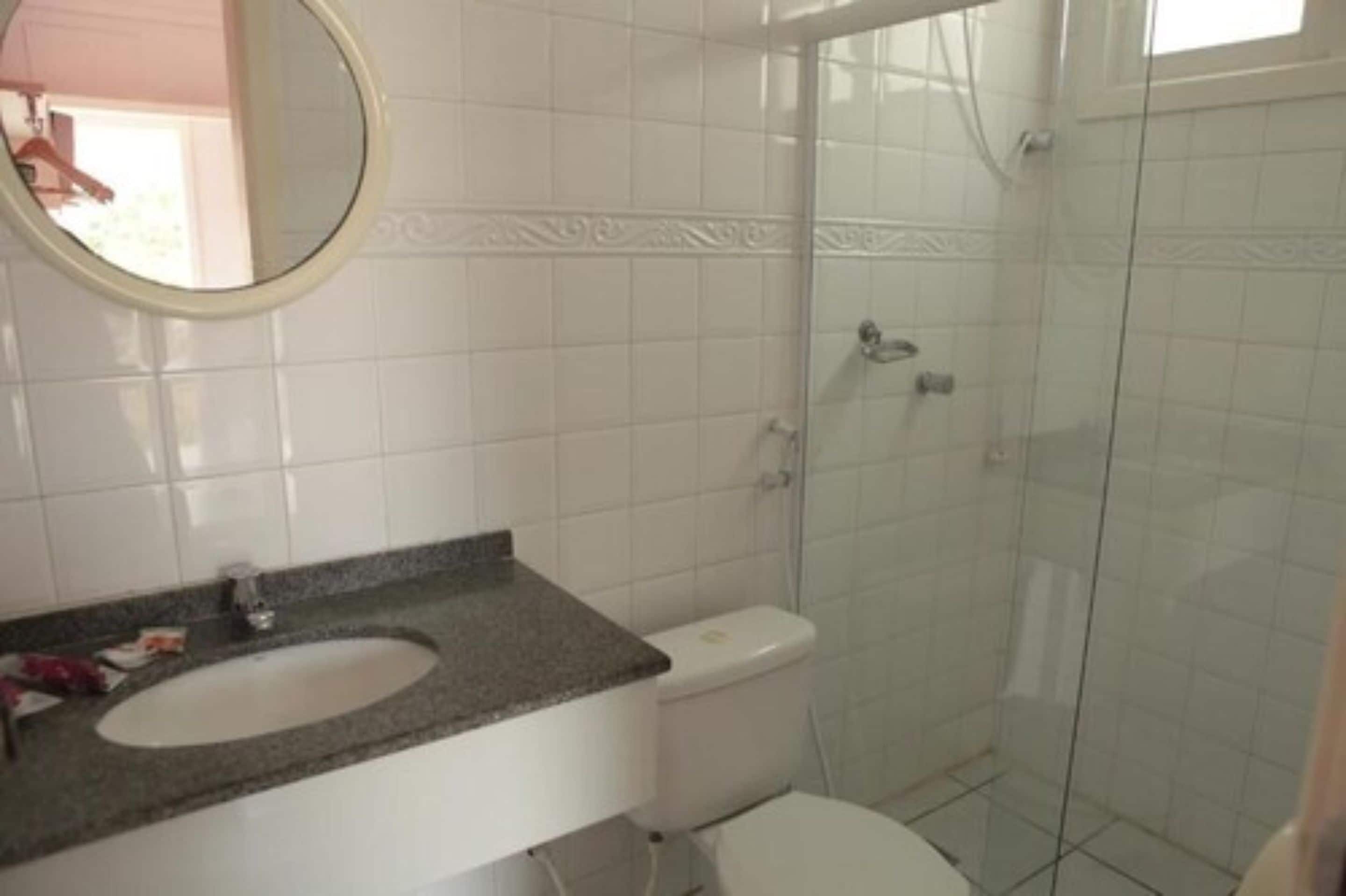 Casa de banho com lavatório branco, sanita e cabine de duche em vidro.