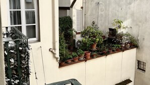 A narrow urban courtyard with potted plants on the balcony, a window with curtains, and a small door. - B & Beatrice (Florence)