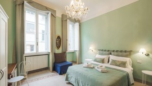 A bedroom with a bed, a chair, a table, and a chandelier. - B & Beatrice (Florence)
