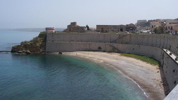 A coastal town with a fortified wall, a beach, and buildings in the background. - Case D'Anna (Castellammare del Golfo)