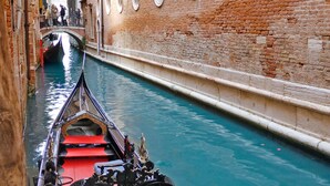 Un canal estrecho con una góndola en primer plano y un puente al fondo.