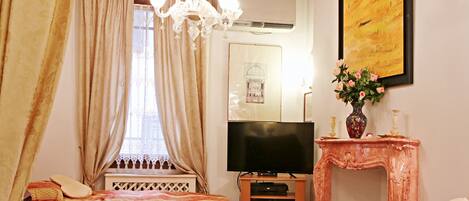 A hotel room with two beds, a TV, a fireplace, and a chandelier.