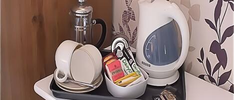 A kitchen area with a coffee maker, a kettle, and a tray with cups and food items.