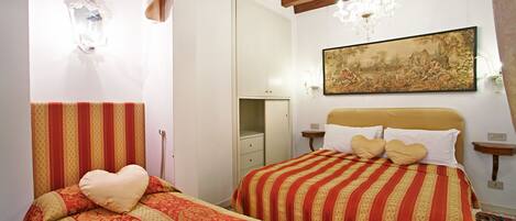 A bedroom with two beds, a chandelier, a painting, and a mirror.