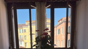 Una habitación con una mesa y sillas de madera, una planta en maceta y un ventanal con vistas a edificios.