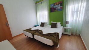 Un lit double avec une couverture marron, des oreillers blancs et un mur vert. Il y a une petite table de chevet avec une lampe.