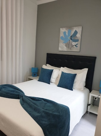 A neatly made bed with white and blue bedding, a dark headboard, and a blue abstract painting on the wall.