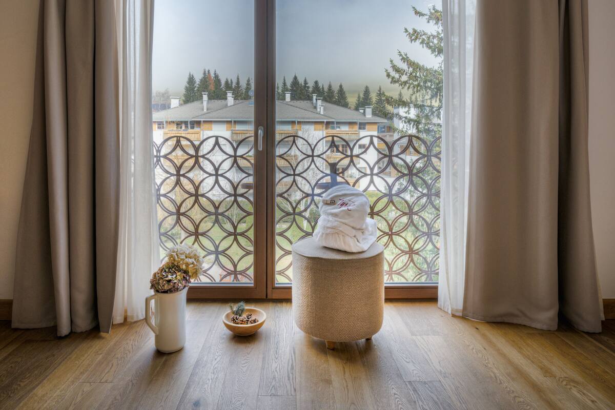 Een kamer met een grote schuifglazen deur die leidt naar een balkon met uitzicht op een woonwijk en bomen.