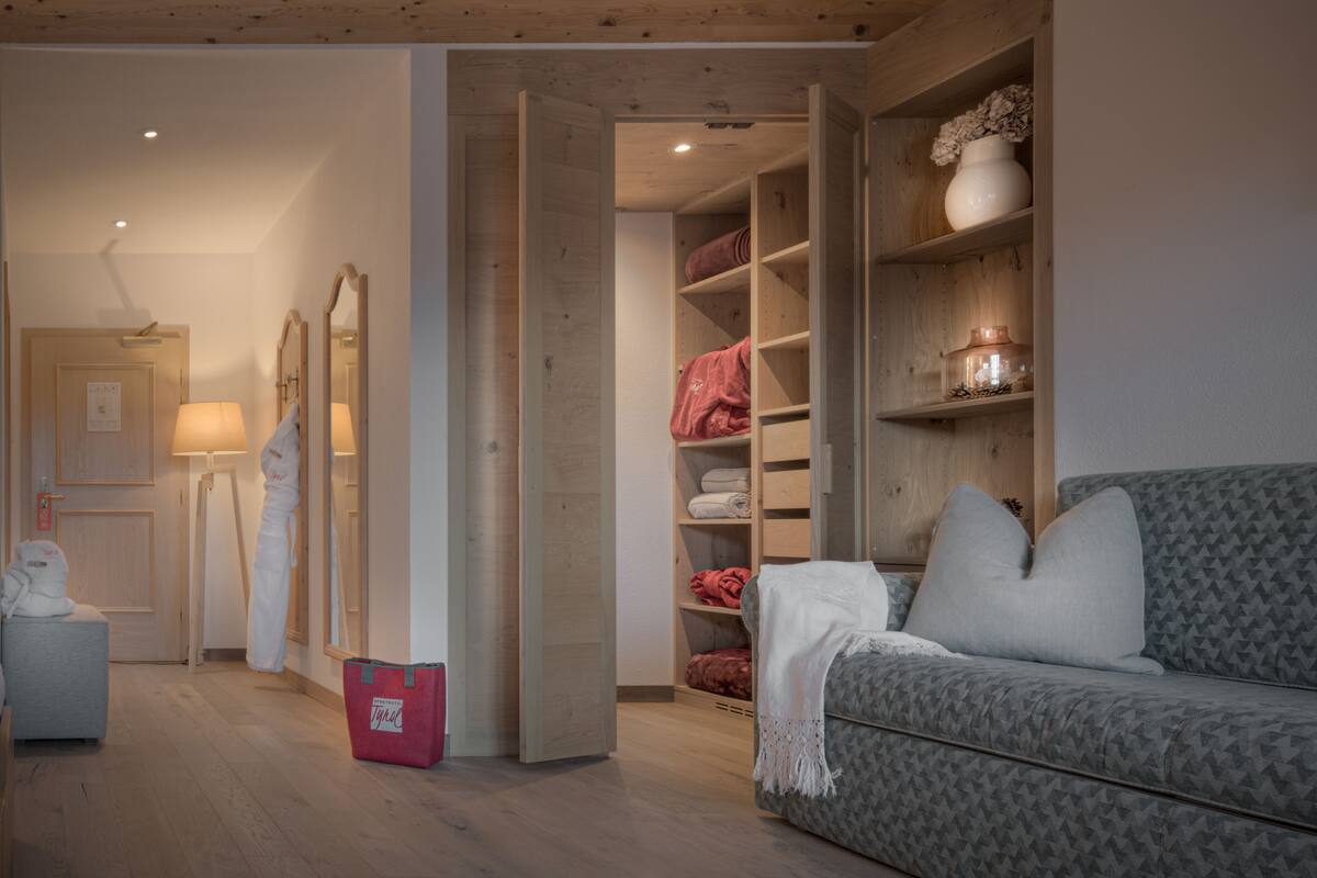 Een knus vertrek met een grijs gestreept sofa, houten planken met handdoeken en een houten plafond.