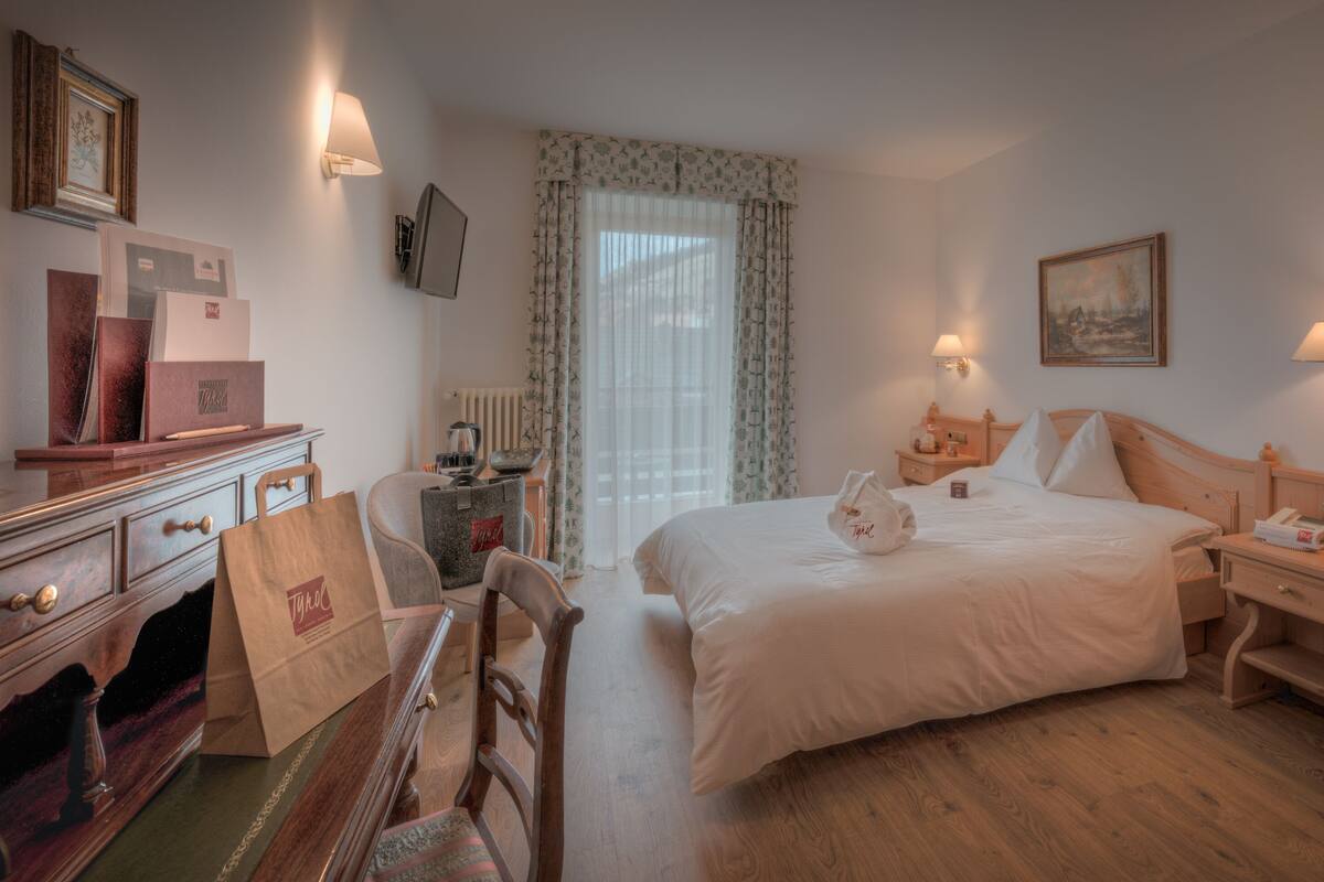 Hotelkamer met een bed, nachtkastjes, een bureau, een stoel, een radiator, een raam met gordijnen en wandlampen.