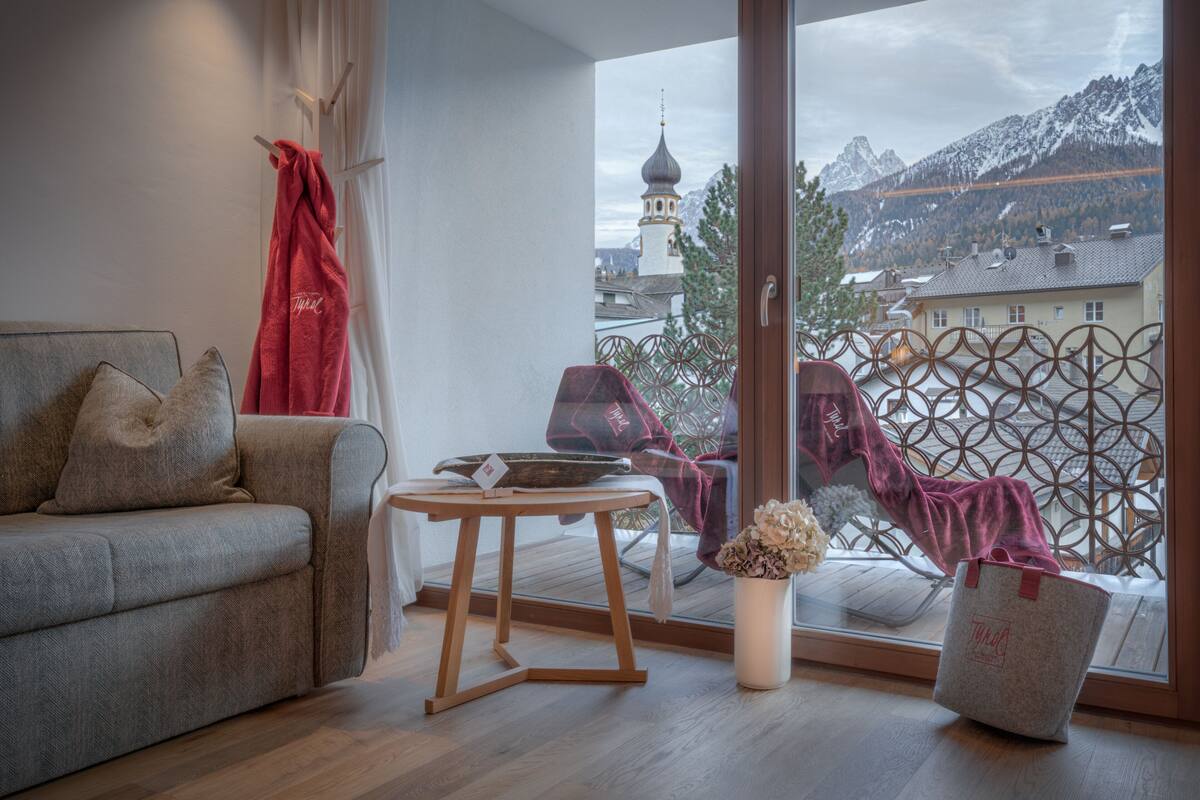 Een moderne woonkamer met een bank, een klein tafeltje en uitzicht op een berglandschap door een groot raam.