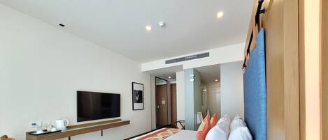 Una habitación de hotel moderna con una cama grande, un televisor de pantalla plana, un escritorio con cafetera y una zona de ducha.