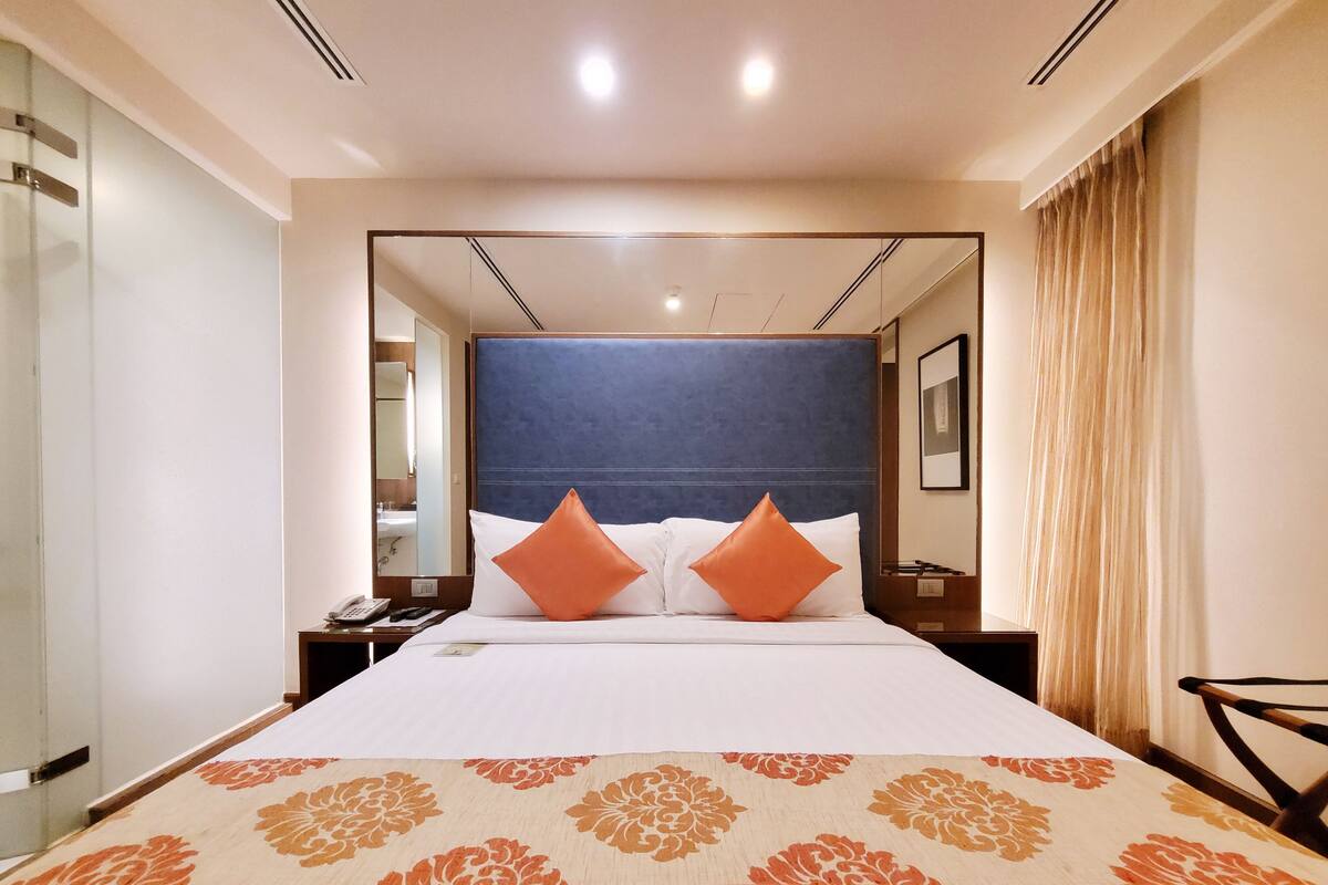 A hotel room with a large bed, two orange pillows, a blue headboard, and a floral-patterned bedspread.