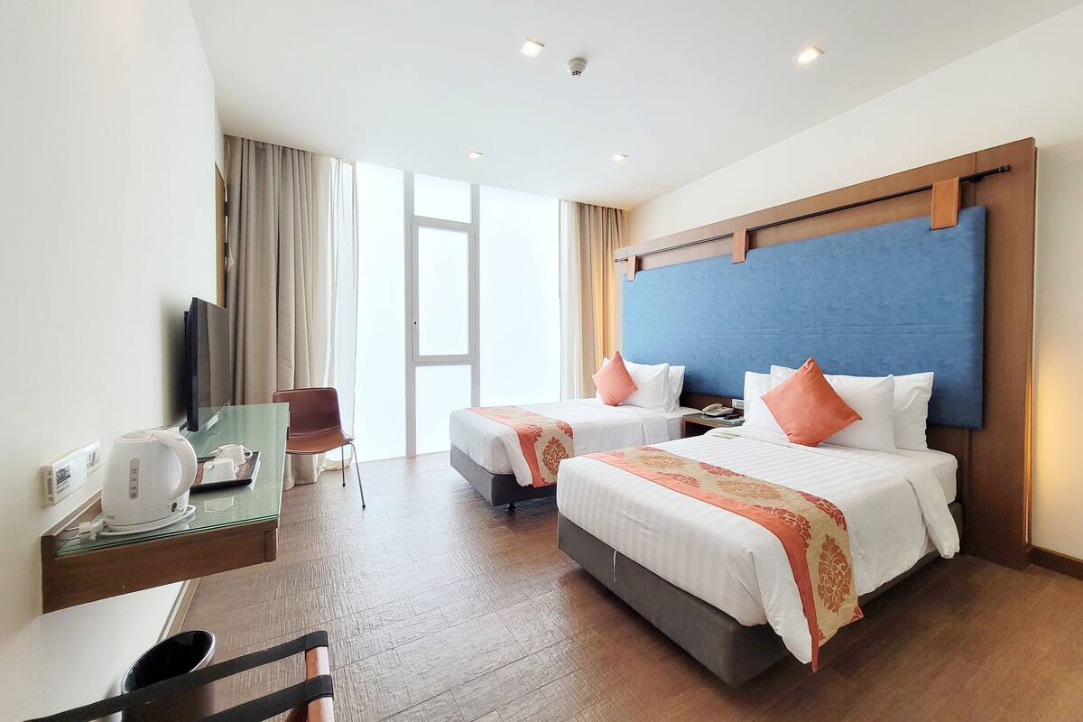 A hotel room with two beds, a desk with a coffee maker, a chair, and a TV.