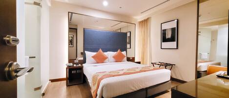 A modern hotel room with a large bed, a bedside table, a mirror, and a view of the adjacent room.