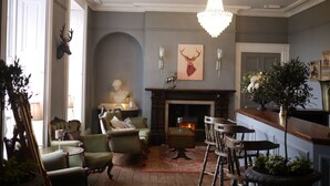 A traditional living room with a fireplace, green armchairs, a wooden coffee table, and a chandelier.