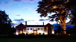 A large, multi-story building with a prominent entrance and multiple windows, surrounded by trees and a well-maintained lawn.