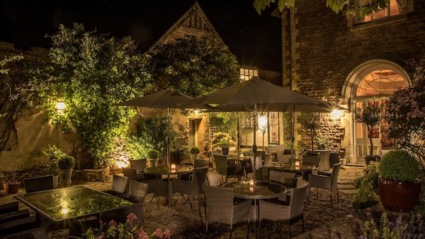 An outdoor patio area with tables and chairs, surrounded by potted plants and a stone wall.