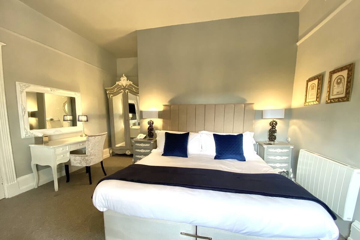 Une chambre d’hôtel avec un grand lit, une coiffeuse avec un miroir, une commode et une armoire.