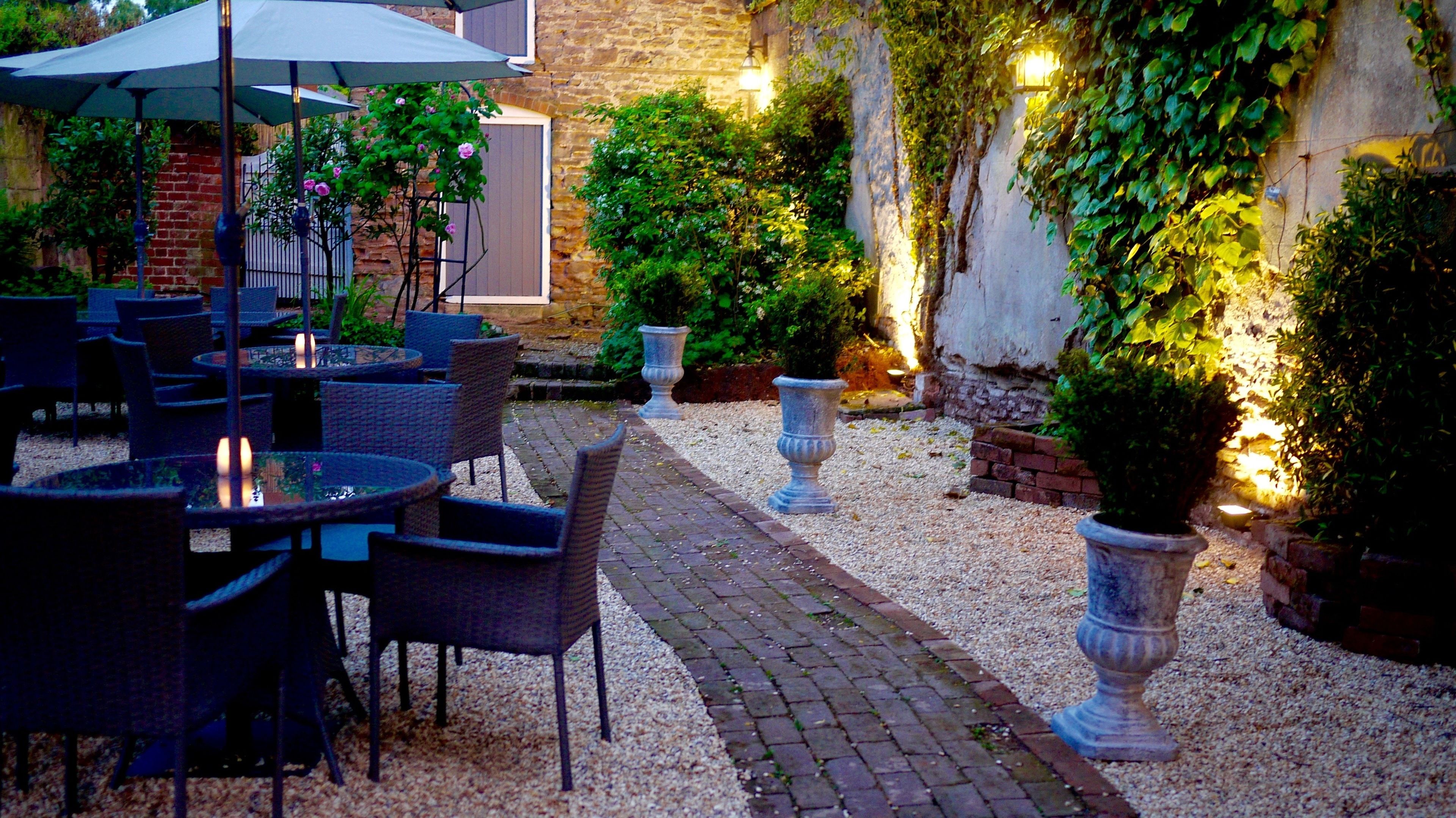 Un espace extérieur aménagé en terrasse, avec des tables et des chaises, entouré de verdure et de murs en pierre.