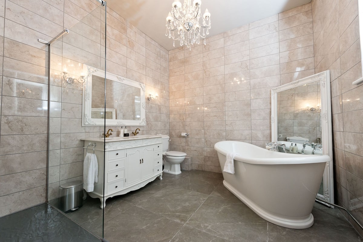Une salle de bain moderne avec une baignoire sur pieds, un meuble-lavabo avec un miroir et un lustre.