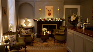 A cozy living room with a fireplace, green armchairs, a coffee table, and a mantel decorated with festive garlands.