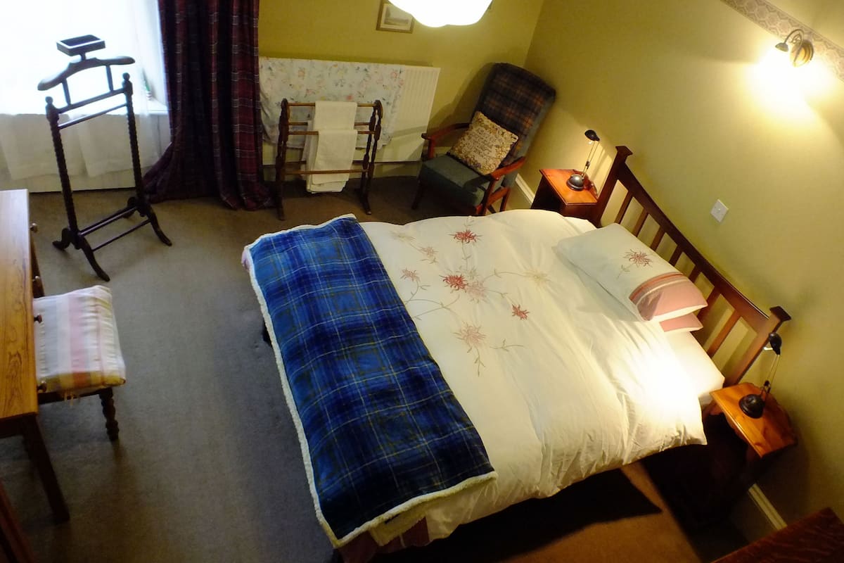 A bedroom with a bed, a chair, a table, and a lamp.