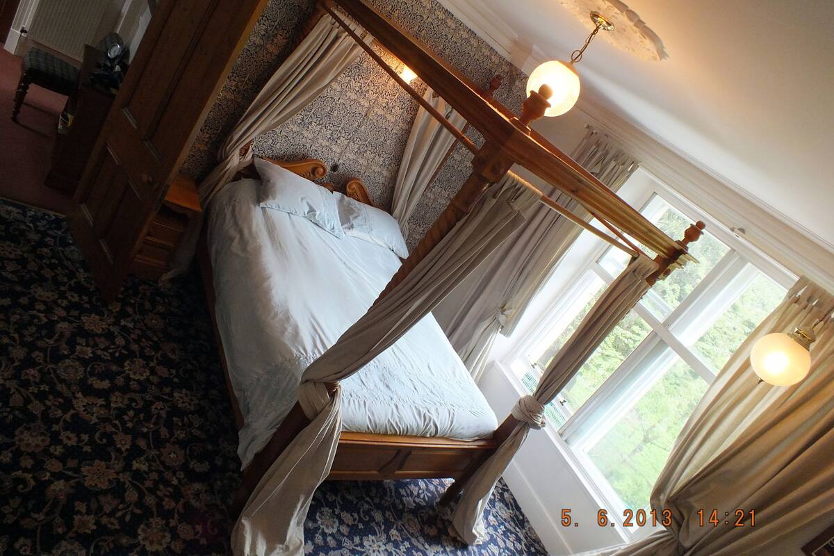 A four-poster bed with a canopy, a wooden dresser, a nightstand, and a window with curtains.