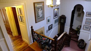 A staircase with wooden railings, a chandelier, and various framed pictures on the walls. - Greystones B&B (Kingussie)