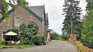 A stone building with a gravel driveway leading to a wooden fence. - Greystones B&B (Kingussie)