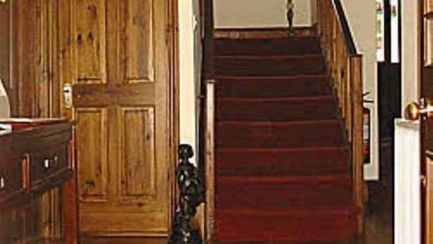 Una escalera de madera con un tapete rojo que sube a un piso superior.