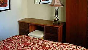 Un dormitorio con una cama, un escritorio de madera, una lámpara, un armario y un cuadro en la pared.