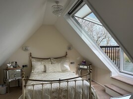 Un dormitorio con techo inclinado, una cama con estructura metálica, un candelabro, mesitas de noche y una ventana con vistas al exterior.