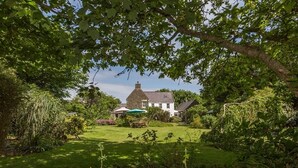 A traditional house with a well-maintained lawn and garden, surrounded by trees and shrubs. - Clos De Vaul Creux (Sark)