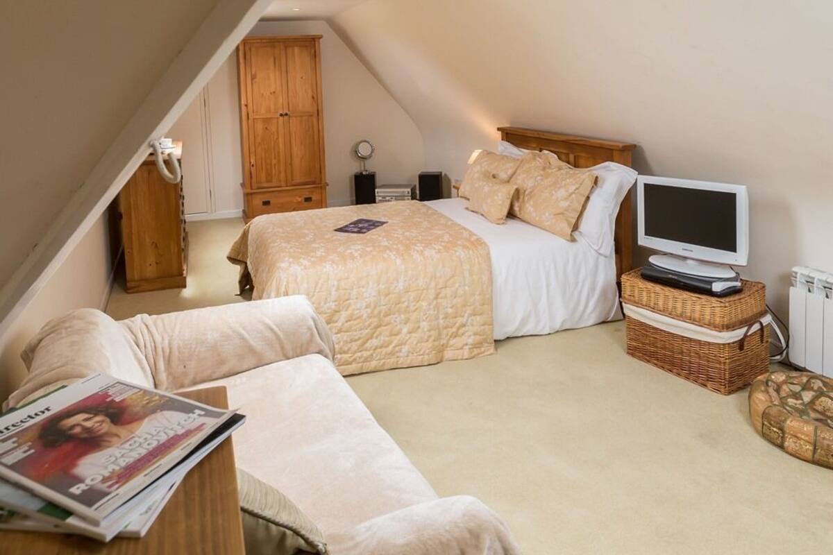 A bedroom with a bed, a television, a wooden wardrobe, and a small table with a magazine.