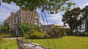 A stone building with a hanging chair in a grassy yard. - Clos De Vaul Creux (Sark)