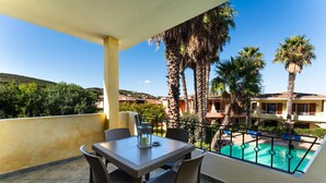 A balcony with a table and chairs, overlooking a swimming pool and a building with palm trees. - Palau Green Village (Palau)