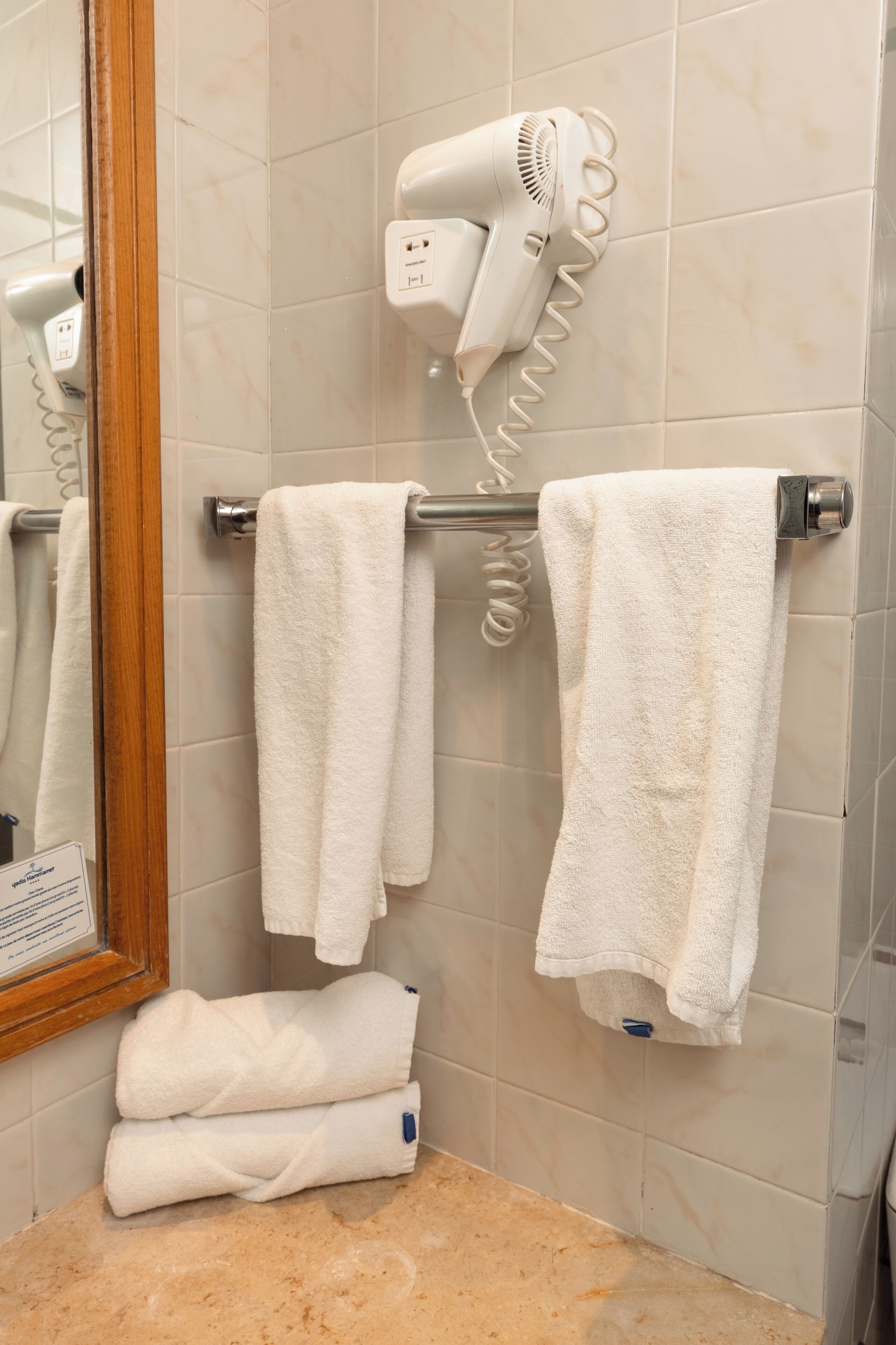 A bathroom with a hairdryer mounted on the wall, a towel rack with towels, and a mirror.