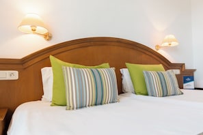 A hotel room with a wooden headboard, two pillows, a nightstand, and a wall-mounted lamp. - Yadis Hammamet Club (Hammamet)