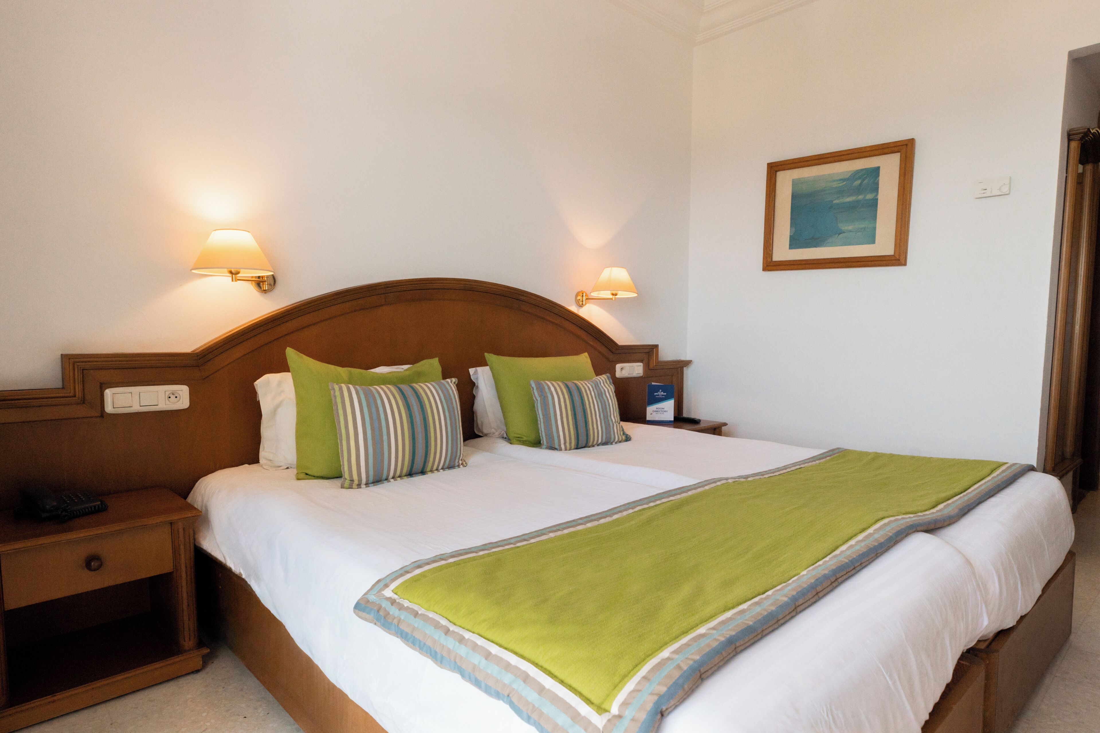 A hotel room with a large bed, two bedside lamps, a nightstand, and a framed picture on the wall.