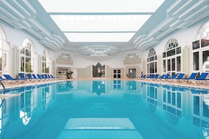 A large indoor swimming pool with blue lounge chairs, large arched windows, and a skylight ceiling. - Yadis Hammamet Club (Hammamet)