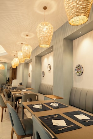 Un ristorante con diversi tavoli e postazioni, lampadari in vimini a soffitto e piatti decorativi appesi alle pareti.